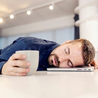 Ein Mann schläft auf seinem Laptop. Was du bei Schlafproblemen tun kannst, verraten wir dir hier!