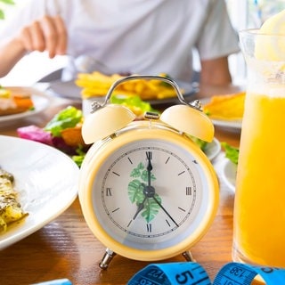 Tisch mit Essen und einer Uhr als Symbol fürs Intervallfasten als angeblich gesunde Alternative zur Ernährung mit Diät.