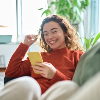 Junge Frau schaut lachend auf ihr Smartphone. Symbolbild für witzige Sprüche im Whatsapp-Status.