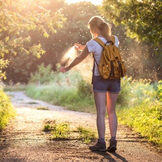 Eine Frau sprüht sich beim Wandern in der Natur ein Mittel gegen Mittel und Zecken auf den Arm. Welche empfiehlt Stiftung Warentest?