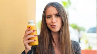 Eine Frau hält einen Saft in der Hand und macht eine Saftkur, bei der sie sich fragt, was sie wirklich bringt.