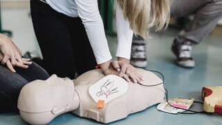 Junge Frau ist über eine Puppe gebeugt und setzt Tipps zur Ersten Hilfe um, indem sie eine Reanimation durchführt