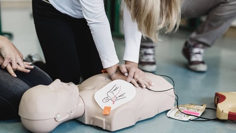 Junge Frau ist über eine Puppe gebeugt und setzt Tipps zur Ersten Hilfe um, indem sie eine Reanimation durchführt