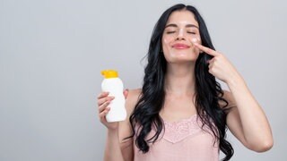Eine Frau vor grauem Hintergrund reibt sich mit Sonnencreme ein. Kann sie sie wiederverwenden?