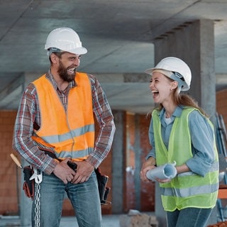 Zwei Baustellen-Kollegen lachen in einem Rohbau über die lustigen Sprüche von der Baustelle. 