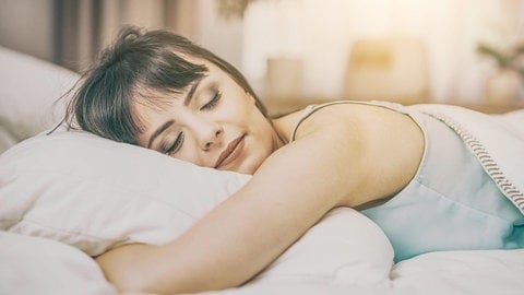 Eine Frau liegt gemütlich auf ihrem Kopfkissen im Bett
