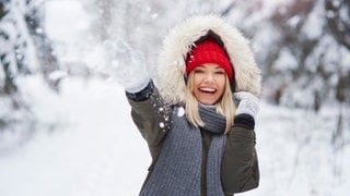 Eine Frau freut sich auf den Winter und wirft mit Schnee.