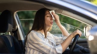 Eine Frau kämpft mit der Hitze im Auto. Sie tupft sich die Stirn mit einem Tuch ab.