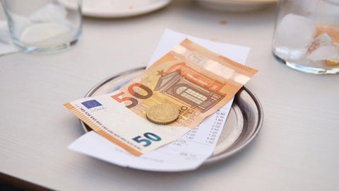 Trinkgeld und Rechnung auf einem Tisch: Wie viel ist im Urlaub angemessen?