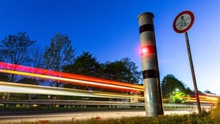 Eine Blitzersäule mit unscharfen Lichtern im Hintergrund.