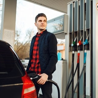Mann steht an der Tankstelle und tankt